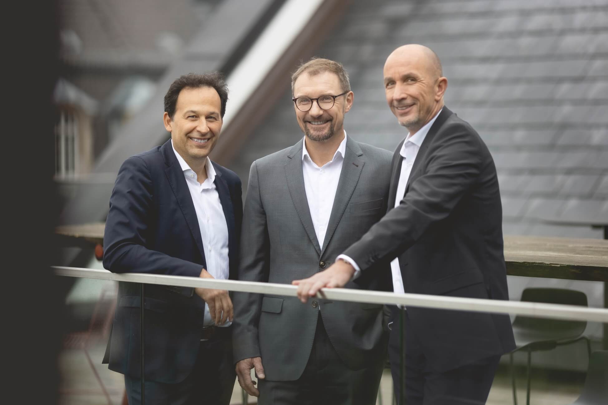Alle 3 HERATAX Partner / Steuerberater Robert Heiss, Oliver Lindloff & Durica Radenovic auf Dachterrasse in Anzügen freundlich lachend