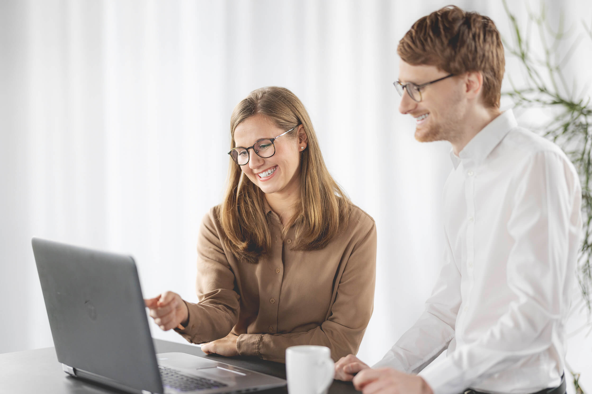 2 Mitarbeiter vor dem PC lächelnd am arbeiten