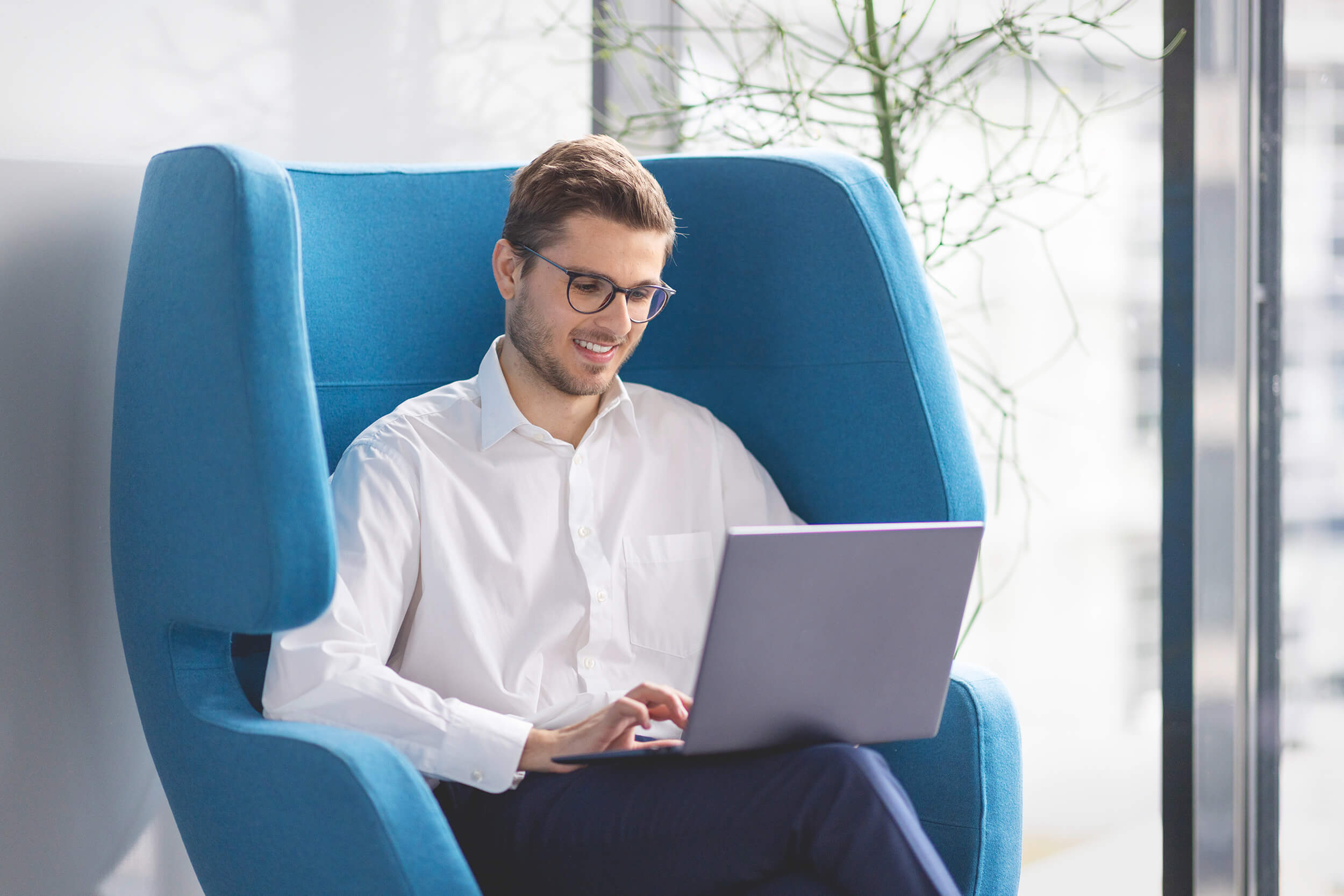 Mitarbeiter im blauen Ohrensessel im Homeoffice am Notebook